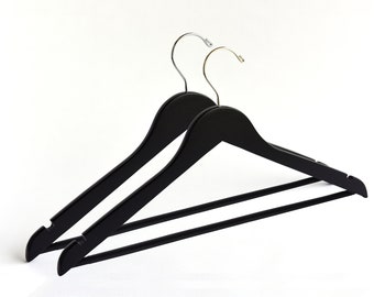 May include: Two black wooden hangers with chrome hooks. The hangers are designed for hanging clothes.