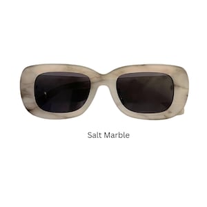 May include: White sunglasses with a marble pattern and dark lenses. The sunglasses are labeled "Salt Marble".