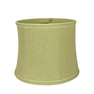 May include: A beige lampshade with a slightly curved shape. The lampshade is made of a textured fabric and has a white trim along the top and bottom edges. The lampshade is designed to fit over a lamp base.