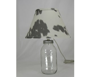 May include: A glass mason jar lamp with a white and grey cowhide patterned lampshade.