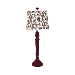May include: A red table lamp with a snowman patterned lampshade. The lamp has a traditional design with a round base and a tall, slender stem.