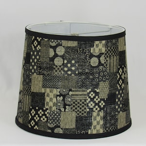 May include: A black and cream lampshade with a patchwork design. The lampshade is made of fabric and has a black trim.