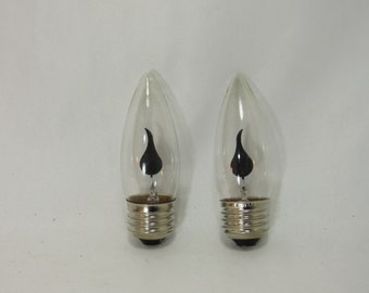 May include: Two clear glass light bulbs with black flame-shaped silhouettes inside. The bulbs have standard screw-in bases.