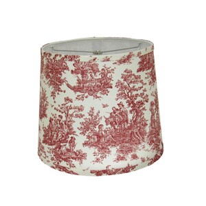 May include: A red and white lampshade with a toile pattern featuring a pastoral scene. The lampshade is made of fabric and has a round shape.