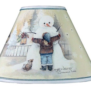 May include: A cream-colored lampshade with a winter scene featuring a snowman, a child, and a dog. The scene is painted in watercolor style with a light blue sky and white snow. The text "Pat Richter... "Snowman Love" is printed on the bottom of the lampshade.