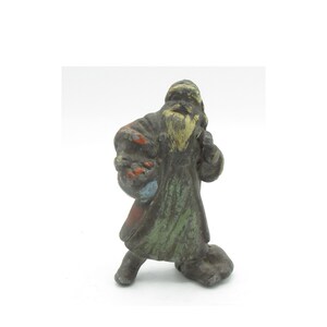 May include: A vintage cast iron figurine of Santa Claus wearing a green and red coat with a white beard. The figurine is painted in shades of green, red, white, and blue.