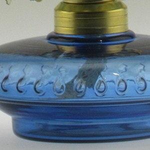 May include: A blue glass oil lamp with a decorative design around the base. The lamp has a brass top and a wick.