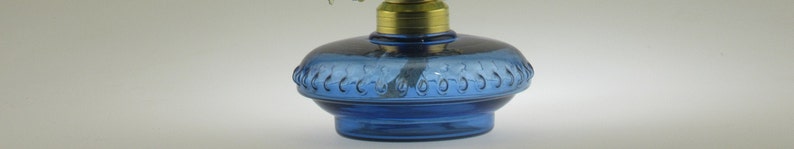 May include: A blue glass oil lamp with a decorative design around the base. The lamp has a brass top and a wick.
