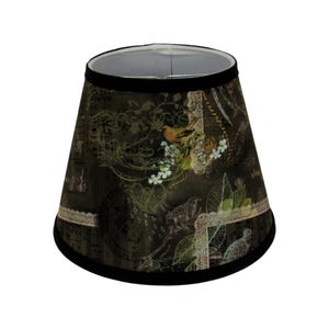 May include: A decorative lampshade with a dark brown background featuring a bird and floral design. The shade has a black trim at the top and bottom, and a white lace-like border. The design includes birds, flowers, and musical notes.