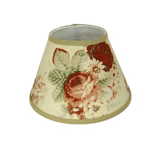 May include: A conical lampshade with a floral design. The shade has a cream-coloured base with large red and pink roses, green leaves, and white flowers. The top and bottom edges are trimmed with a tan fabric.