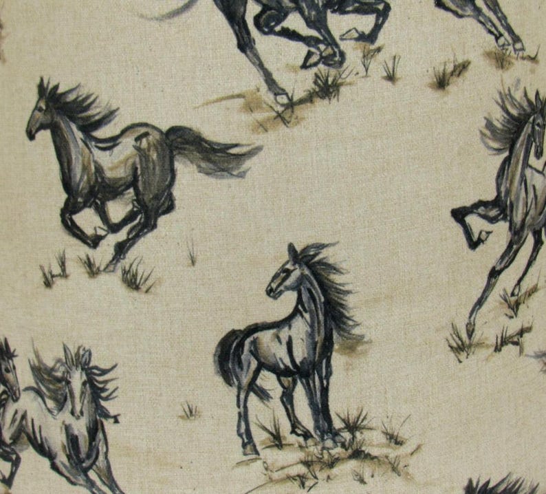 Op de afbeelding: Een herhalend patroon van rennende paarden in grijstinten en zwart op een beige achtergrond. De paarden zijn afgebeeld in een aquarel stijl, met vloeiende manen en staarten. Het ontwerp bevat kleine plukjes gras.
