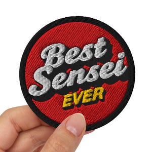 Peut inclure: Un écusson rond brodé avec un fond rouge et les mots "Best Sensei Ever" en blanc et jaune. L'écusson est tenu par une main sur un fond blanc. L'écusson mesure environ 7,6 cm de diamètre.
