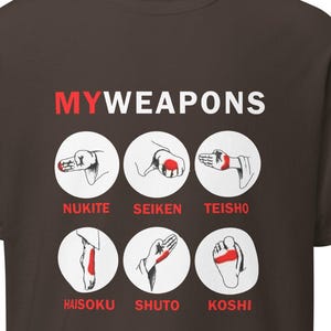 May include: A brown t-shirt with the text "MY WEAPONS" in red letters. The shirt features six illustrations of different karate strikes and kicks, each with a red circle highlighting the striking point. The illustrations are labeled with the Japanese names for each strike: "NUKITE", "SEIKEN", "TEISHO", "HAISOKU", "SHUTO", and "KOSHI".