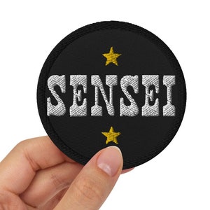 Peut inclure: Un patch rond noir avec du texte brodé blanc qui dit "SENSEI" et deux étoiles brodées dorées.