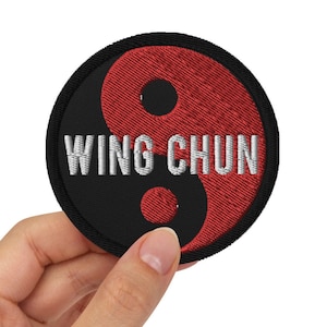 Op de afbeelding: Een geborduurde zwarte en rode patch met een yin yang symbool en de tekst "WING CHUN" in wit.