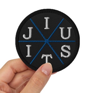 Pode incluir: Um remendo redondo preto com letras bordadas brancas que soletram "JIU Jitsu" em um círculo. As letras são conectadas por costuras azuis.