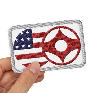 May include: A white embroidered patch with a red, white, and blue American flag on the left and a red circle with a white center and four red points on the right.