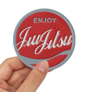 May include: A red and gray embroidered patch with the text "ENJOY Jiu Jitsu" in white.
