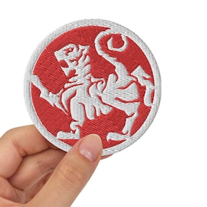 Könnte beinhalten: Ein roter gestickter Aufnäher mit einem weißen Löwenmotiv. Der Löwe steht auf seinen Hinterbeinen mit hochgekrülltem Schwanz.