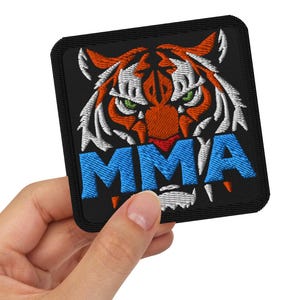 Puede incluir: Un parche bordado negro con la cara de un tigre y la palabra "MMA" en letras azules.