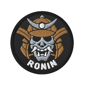 Puede incluir: Un parche bordado en blanco y negro con una calavera de samurái que lleva un casco marrón. El texto "RONIN" está escrito debajo de la calavera.