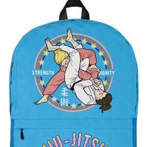 May include: A light blue backpack featuring a Jiu-Jitsu design. The backpack has a front pocket and black straps. The design includes illustrations of two people in a Jiu-Jitsu match, the words "Strength, Dignity", and "Jiu-Jitsu Fighter".