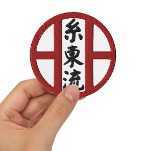 Puede incluir: Un parche circular rojo con un centro blanco y un símbolo japonés negro que se lee "行雲流水" (pronunciado "gyoun unryu") que se traduce como "nubes fluidas y agua corriente".