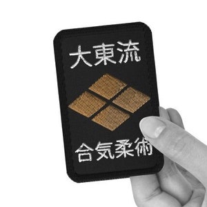 May include: Black embroidered patch with white text that reads "大東流 合気柔術". The patch features a stylized brown diamond shape.