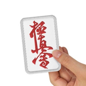 May include: A white mahjong tile with a red Chinese character on it.