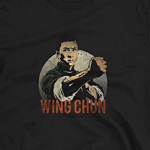 May include: Black t-shirt with a graphic of a man in a black martial arts uniform with the text "Wing Chun" printed below.