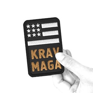 May include: Black embroidered patch featuring a white American flag and the words "KRAV MAGA" in gold thread.