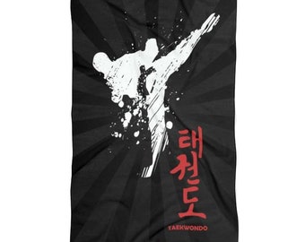 May include: Black beach towel featuring a white silhouette of a person performing a taekwondo kick. The background has a sunburst pattern. The text "Taekwondo" is written in red below the silhouette.