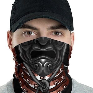 Pode incluir: Uma m&aacute;scara facial preta com um design de capacete de samurai vermelho e branco. O capacete tem uma express&atilde;o amea&ccedil;adora com uma boca grande e dentes afiados. A m&aacute;scara &eacute; feita de um tecido macio e respir&aacute;vel e &eacute; perfeita para o uso di&aacute;rio.