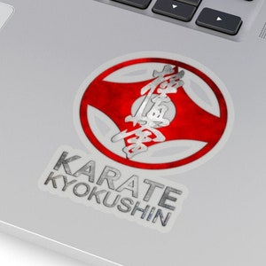 May include: A red and white circle sticker with silver lettering that says "Karate Kyokushin". The circle has a red background with a white center and a silver outline. The lettering is in a bold, sans-serif font.