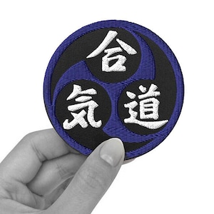 Puede incluir: Un parche bordado negro y azul con tres caracteres japoneses blancos: "合気道" (Aikido).