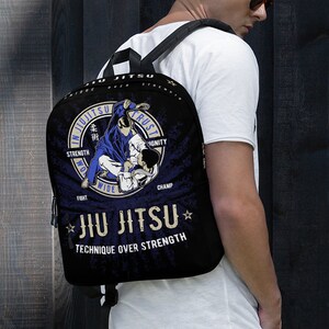 May include: Black backpack with a blue and white Jiu-Jitsu design. The design features a figure in a blue gi performing a submission hold. The text on the backpack reads "In Jiu-Jitsu Trust", "Strength Over Strength", "Fight Wide", "Champ", "Jiu-Jitsu", and "Technique Over Strength".