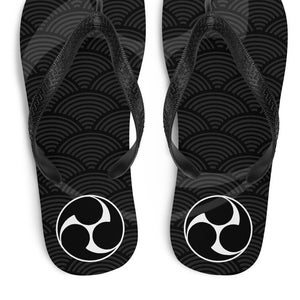Puede incluir: Chanclas negras con un patrón de olas japonesas blancas y un símbolo blanco de tres círculos en la parte inferior.