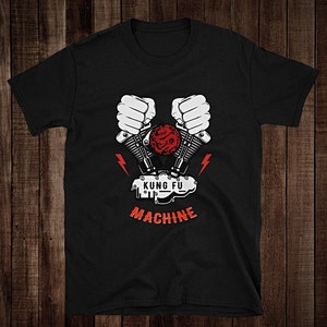 Puede incluir: Camiseta negra con un gráfico blanco de un motor de motocicleta con puños sosteniendo los pistones. El texto "Kung Fu Machine" está impreso debajo del motor.