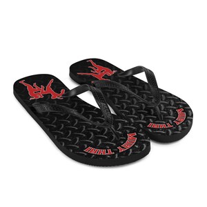 May include: Pair of black flip flops with a red Muay Thai logo and silhouette of two fighters. The flip flops have a textured tread pattern.