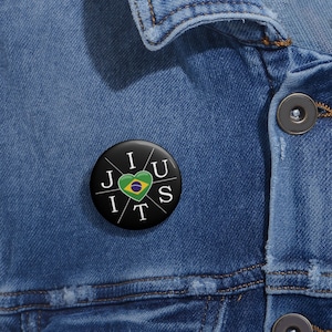 May include: A black button with white lettering that reads "I Jiu Jitsu" with a heart in the middle featuring the Brazilian flag.