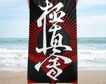 May include: Black beach towel featuring a red and black geometric pattern and white Japanese characters. The towel is displayed against a beach background with a blue sky and sea.