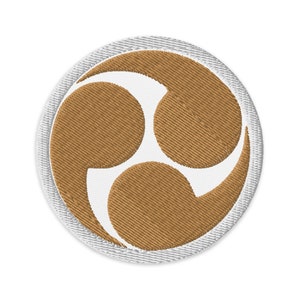 Peut inclure: Un écusson brodé blanc avec un symbole brun à trois parties, ressemblant à un symbole yin-yang stylisé, sur un fond blanc.