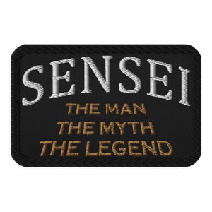 Peut inclure: Écusson brodé noir avec du texte blanc qui dit "Sensei" et du texte marron qui dit "The Man The Myth The Legend".