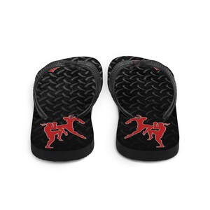 May include: Pair of black flip flops with a diamond plate pattern. The flip flops have a red silhouette of two people in a fighting stance.