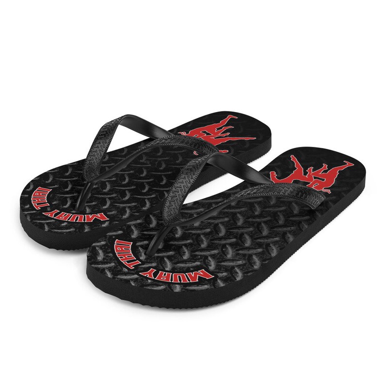 May include: Pair of black flip flops with a red "Muay Thai" logo and a silhouette of two fighters. The flip flops have a textured tread pattern.
