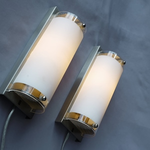 May include: Two silver wall sconces with frosted glass shades. The sconces have a modern design and are illuminated with warm white light.