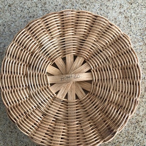 May include: A round, woven wicker basket with a circular, open center. The basket has a brown, natural finish and the center has a handwritten inscription that reads "B2H 20".