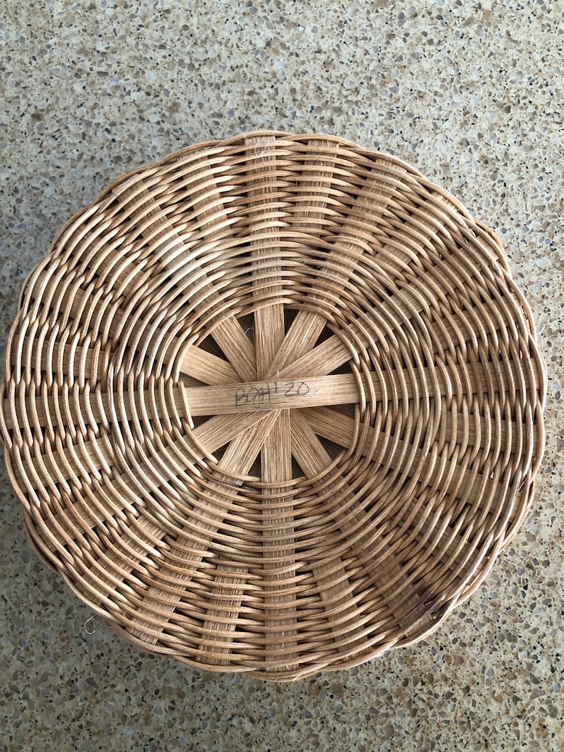 May include: A round, woven wicker basket with a circular, open center. The basket has a brown, natural finish and the center has a handwritten inscription that reads "B2H 20".