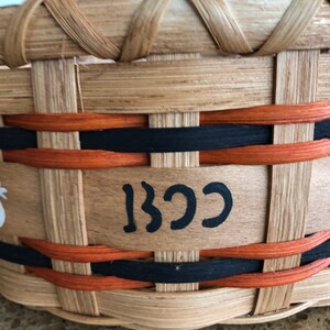 May include: A woven basket with black and orange trim. The basket has a wooden base with the word "BCC" written in black paint.