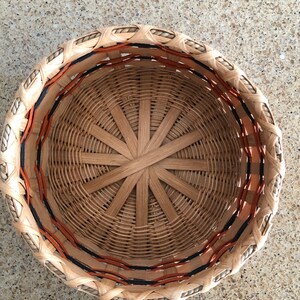 May include: A woven basket with a brown and orange rim. The basket is made of natural materials and has a circular shape.